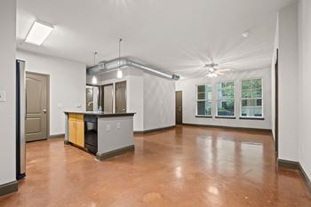 An empty living room with a kitchen and a large window
